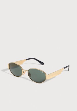 Lunettes de soleil Vogue dorées, avec des verres ovales vert foncé et des branches aux extrémités noires, sur un fond uni clair.