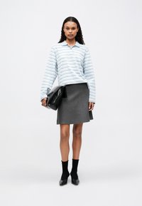 Hellblau gestreiftes Polohemd mit langen Ärmeln, kombiniert mit einem grauen, taillierten Rock. Eine schwarze Clutch und Socken runden den Look ab.