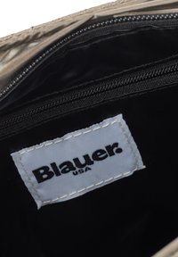 Weißes Stoffetikett mit der Aufschrift "Blauer USA" in schwarzer Stickerei in einem schwarzen Reißverschlussfach einer Tasche.
