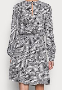 Robe à motif pied-de-poule noir et blanc, avec des manches longues, un dos en trou de serrure, une taille cintrée et une jupe évasée avec un ourlet en couches.