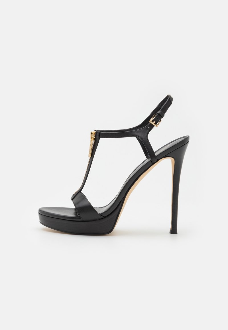 Sandale à plateforme noire à talons hauts avec fine bride à la cheville, détail fermeture éclair à l'avant et boucle dorée sur fond blanc.