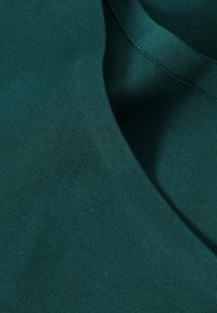 Dark green cotton fabric with a smooth texture, featuring a wide neckline and subtle stitching detail. The material appears lightweight and flexible.