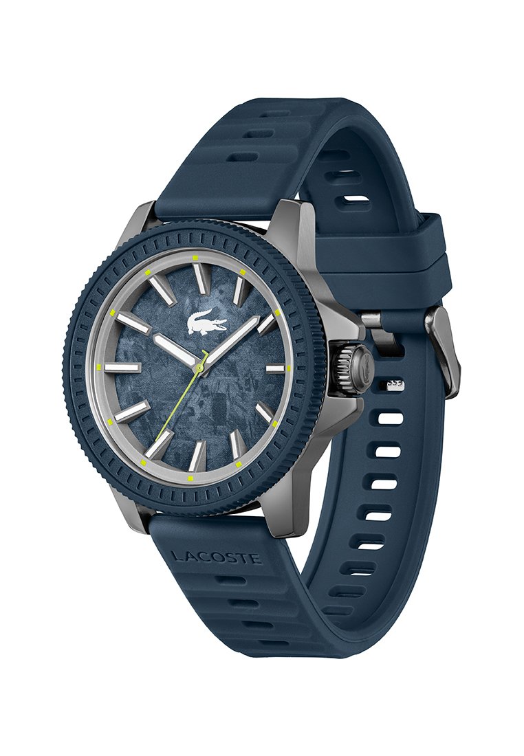 Montre avec un bracelet en silicone bleu marine, cadran texturé bleu marine, accents argentés, aiguilles lumineuses et lunette grise avec des marqueurs jaunes.