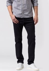 Jeans de mezclilla azul oscuro con corte recto, costuras en contraste y una textura suave, combinados con zapatillas blancas.