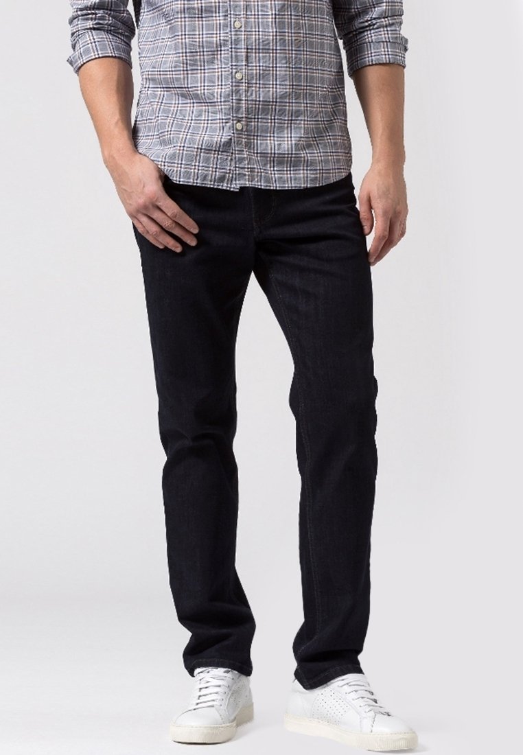 Jeans de mezclilla azul oscuro con corte recto, costuras en contraste y una textura suave, combinados con zapatillas blancas.