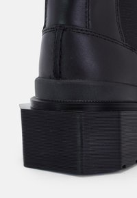 Gros plan sur une botte en cuir noir avec une semelle plateforme épaisse et striée et des détails cousus au niveau du talon.