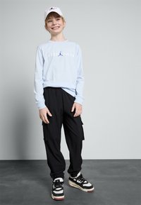 Lys blå langermet skjorte med "JORDAN"-logo, svarte cargo-bukser med lommer, og svarte sneakers med hvite og røde detaljer.