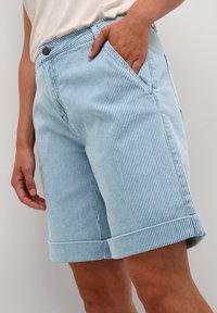 Pantaloni corti a righe azzurri realizzati in tessuto testurizzato, con tasche laterali e orlo risvoltato. La vita è dotata di chiusura con bottone metallico.