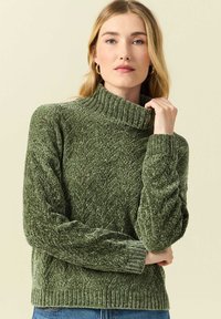 Grön stickad tröja med hög polokrage, med ett strukturerat fiskbensmönster och ribbade mudd och fåll.