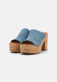 Mule sandali aperti in denim blu con tacco a blocco in sughero, caratterizzati da una texture liscia e un design della parte superiore ampia e curva.