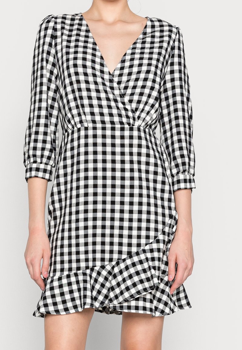 Robe à carreaux vichy noir et blanc avec un décolleté en V profond, des manches trois-quarts et un ourlet à volants. Confectionnée en tissu léger.