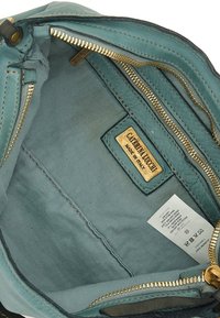 Interno di una borsa in pelle turchese con zip dorata, dotato di più scomparti e un'etichetta che recita "Caterina Lucchi, Made in Italy."