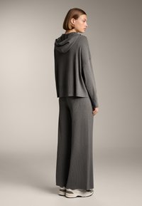 Grauer Strick-Hoodie mit relaxed fit, gerippter Textur und angenähter Kapuze. Kombiniert mit passenden weiten Hosen und Sneakers.