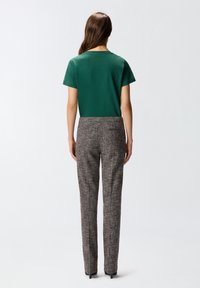 Zeleni kratki rukavani top s okruglim izrezom u kombinaciji s sivim uzorkovanim krojenim hlačama, koje imaju uski kroj i suptilnu teksturu.