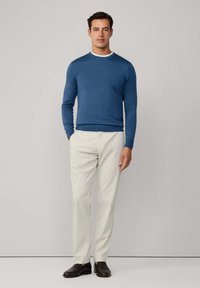 Blauer Pullover mit Rundhalsausschnitt, kombiniert mit hellbeigen Hosen. Das Outfit wird mit dunkelbraunen Schuhen abgerundet. Angenehme, glatte Textur.