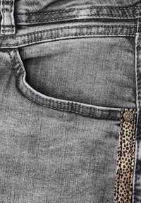Jeans de mezclilla gris con una raya lateral con patrón, con un bolsillo frontal y cierre de botón metálico. La tela tiene un acabado suave y texturizado.