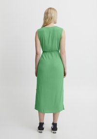 Rochie verde făr�ă mâneci, cu talie ajustată, lungime până la genunchi și buzunare laterale. Purtați-o cu adidași negri cu accente albe.