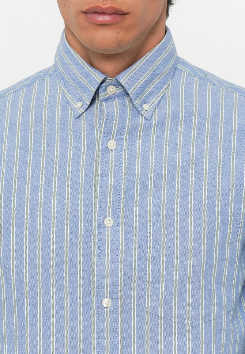 Jasnoniebieska koszula zapinana na guziki z białymi i zielonymi pionowymi paskami, kołnierzykiem oraz jedną kieszenią na piersi, wykonana z gładkiego materiału.