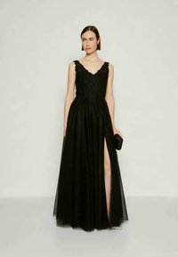 Vestido de noite preto com um corpete justo e bordado, alças rendadas e uma saia de tule esvoaçante com uma fenda alta na coxa. Carteira combinando.