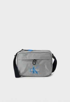 Grå nylon skuldertaske med blå logo, lynlåslukning og justerbar sort rem. Har en lille løkke og synlige syninger som detaljer.