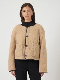 Beige fleece jacket with a boxy shape, black button closure, two front pockets, and contrast stitching along the edges.