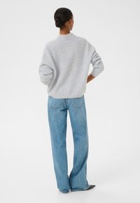 Hellgrauer, gerippter Pullover mit hohem Kragen, kombiniert mit locker sitzenden blauen Jeans aus Denim, die gerade geschnitten sind und Gesäßtaschen haben.