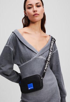 Black crossbody bag with a blue square accent, featuring a patterned strap with "KARL" text. Made from smooth material with a zipped closure.