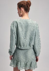 Mintgrön klänning och toppset med intrikata blommönster, långa ärmar och en volangkant. Mjuk textur och lätt material.