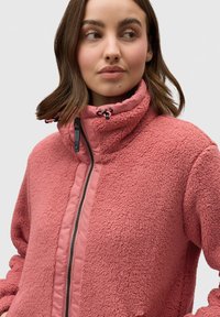Giacca in pile di un rosa morbido, con colletto alto, zip completa e pannelli laterali lisci a contrasto. Presenta lacci regolabili sul colletto.
