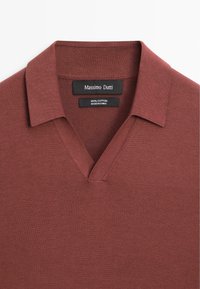 Bavlněný pulovr v hlubokém červeno-hnědém odstínu. Má výstřih do V a krátké rukávy. Hladká textura s minimálními detaily.