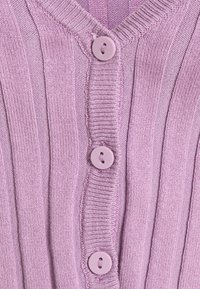 Närbild av lila ribbadhämat tyg med tre matchande runda knappar fästa på ett plagg med V-hals.