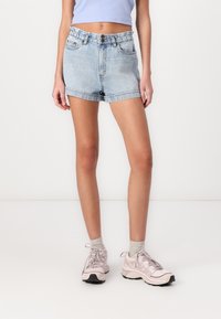 Shorts di jeans con un lavaggio azzurro chiaro, vita alta, orli arrotolati e tasche frontali, abbinati a scarpe sportive rosa chiaro e calze grigie.
