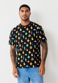 Sort t-shirt med korte ærmer, der har farverige julepyntsmønstre i rød, grøn, blå og gul på en sort baggrund.