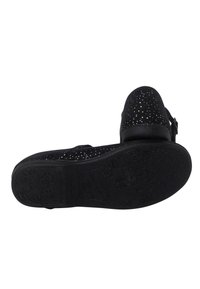 Zapato negro de tipo slip-on con un empeine texturizado que presenta pequeños recortes y destellos. Suela de goma con detalles de patrón floral.