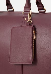 Maroon handbag made of textured synthetic leather with gold hardware, featuring a zippered pocket and an attached card holder.