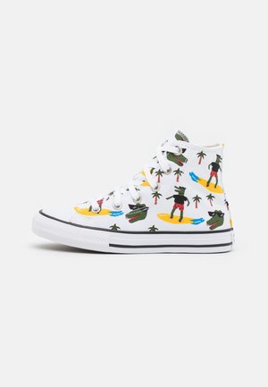 Witte hoge sneaker met cartoonalligatoren die rode shorts dragen en surfen bij palmbomen, witte veters en een zwarte streep op de zool.