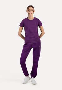 Lilla bomulds t-shirt og matchende sweatpants, slim fit design, rund halsudskæring, diskret branding, parret med hvide sportssko.