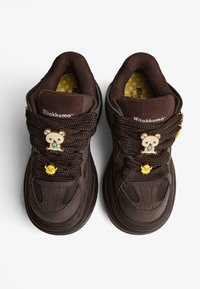 Tmavohnedé tenisky s hrubými šnúrkami, zdobené medvedíkom Rilakkuma a malými žltými kuriatkami, na bielom pozadí.