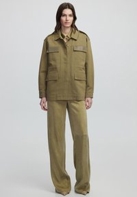 Chaqueta militar de color verde oliva con hombreras texturizadas, dos bolsillos frontales y pantalones de pierna ancha a juego con dobladillos decorados.