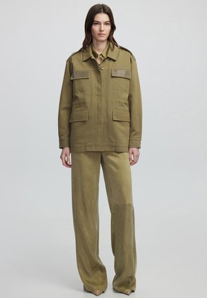 Veste militaire vert olive avec épaulettes texturées, deux poches avant et un pantalon large assorti avec des ourlets à motifs.
