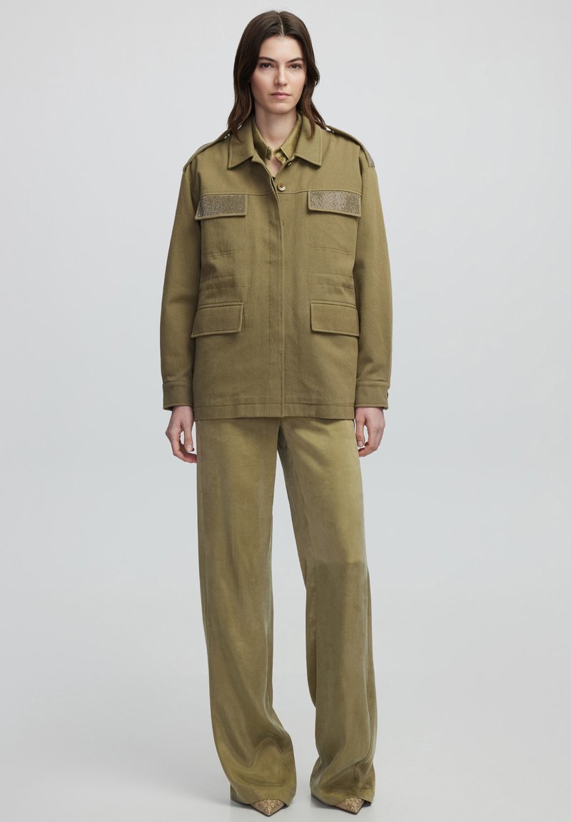 Chaqueta militar de color verde oliva con hombreras texturizadas, dos bolsillos frontales y pantalones de pierna ancha a juego con dobladillos decorados.