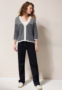 Randig cardigan i marinblått och cream med V-urringning, prydd med knappar fram, ihop med mörka jeans och vita sneakers.