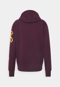 Sudadera con capucha color granate con cordón, puños y dobladillo acanalados. Presenta un diseño decorativo amarillo en la manga izquierda. Tejido de textura suave.