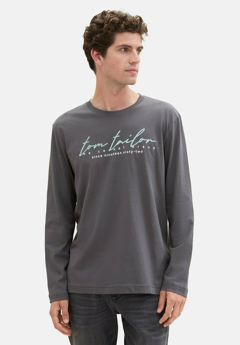 Gray long-sleeve t-shirt made of soft fabric, featuring white and teal printed text: "tom tailford" and "since nineteen sixty-two."
