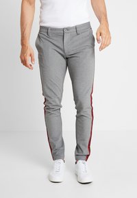 Szare spodnie o wąskim kroju z czerwonymi paskami po bokach. Wykonane z fakturowanej tkaniny, z zapięciem na guziki i przednimi kieszeniami. Połączone z białymi trampkami.