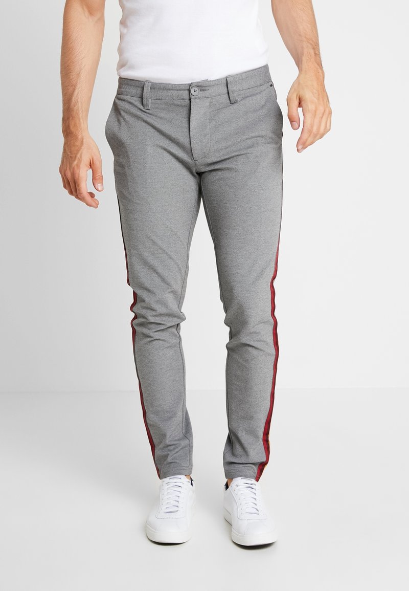 Szare spodnie o wąskim kroju z czerwonymi paskami po bokach. Wykonane z fakturowanej tkaniny, z zapięciem na guziki i przednimi kieszeniami. Połączone z białymi trampkami.