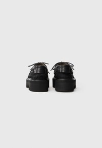 Zwarte leren schoenen met een gestructureerde afwerking, voorzien van een ronde neus, platte veters en een dikke zool. Achterste branding detail zichtbaar.