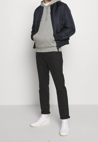 Giacca bomber navy, felpa grigia con cappuccio, pantaloni neri e sneakers bianche. Tessuto morbido, polsini a costine, vestibilità rilassata e design stratificato.