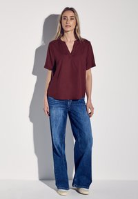 Bordeaux kortärmad topp med V-ringning; parat med vida blå denimjeans. Slät tyg med en lös passform, minimalt med detaljer.