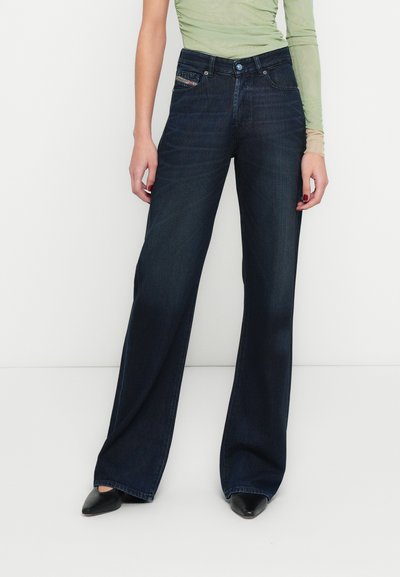 Jean large bleu foncé à taille haute, confectionné en tissu denim. Dispose d'une fermeture à boutons à l'avant et d'un détail de poche décoratif.